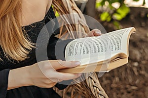 female hands holding a vintage book. girl reading a book sitting on a straw chair