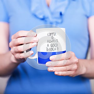 Female hands holding white blue cup with inscription. Coffee is always a good idea. Break time concept