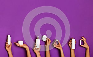 Female hands holding white cosmetics bottles - lotion, cream, serum on violet background. Square crop. Skin care, pure beauty, photo