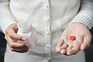 Female hands is holding a white pill bottle and a red pill in he