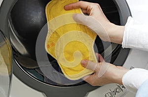 Female hands holding a yellow cloth pad inside a washing machine full of cloth bamboo washable sanitary napkins