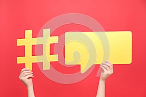 Female hands holding yellow paper hashtag symbol and speech bubble, hash sign of famous media content, isolated on red color