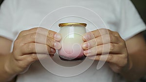 Female hands holds a glass jar of fresh tasty yogurt by removing the golden foil lid in kitchen, closeup.