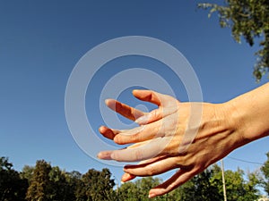 Female hands imitate holding a ball or catch something, isolated against a blue sky background. Girl performs movements with her