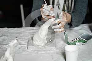 Female hands with an instrument gracefully shape a small plaster sculpture.