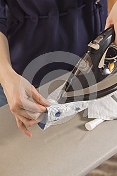 Female hands iron the shirt sleeve on a stand on an ironing board. Ironed clothes lie on the table in the background.