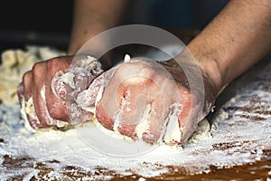 Female hands kneading a flour dough by rolling it on a wooden board