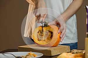 Female hands with knife chopping pumpkin on cutting board. Preparing autumn vegetables.