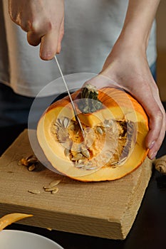 Female hands with knife chopping pumpkin on cutting board. Preparing autumn vegetables. Healthy organic vegetarian food