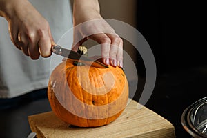 Female hands with knife chopping pumpkin on cutting board. Preparing autumn vegetables. Healthy organic vegetarian food