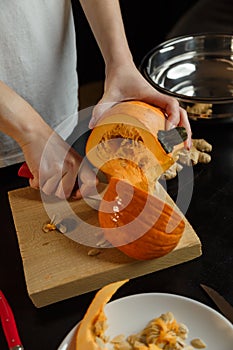 Female hands with knife chopping pumpkin on cutting board. Preparing autumn vegetables. Healthy organic vegetarian food