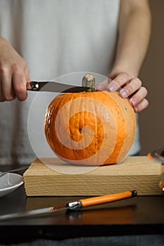 Female hands with knife chopping pumpkin on cutting board. Preparing autumn vegetables. Healthy organic vegetarian food