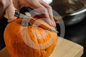 Female hands with knife chopping pumpkin on cutting board. Preparing autumn vegetables. Healthy organic vegetarian food