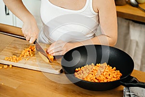 Female hands with a knife cut fresh carrots in the kitchen