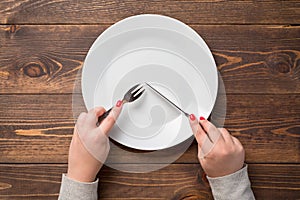 Female hands with knife and fork over white empty plate. Wooden table