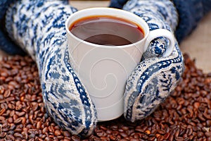 Female hands in knitted mittens holding a mug of hot coffee