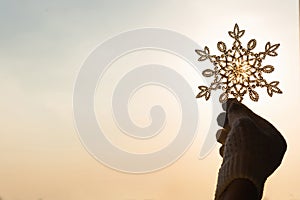 Female hands in a knitted mittens with sparkling huge snowflake on a sunset sky background.