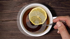 Female hands in a knitted sweater hold a cup of tea with lemon and stir it with a spoon.Close-up.