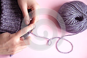 Female hands with knitting needles to knit wool violet sweater on pink background
