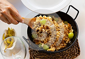 Female hands ladling Migas del pastor with grapes into plate