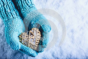 Female hands in light teal knitted mittens with entwined beige flaxen heart on a white snow background. St. Valentines Day concept photo