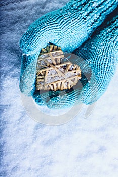 Female hands in light teal knitted mittens with entwined beige flaxen heart on a white snow background. St. Valentines Day concept photo