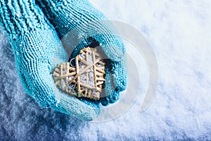 Female hands in light teal knitted mittens with entwined beige flaxen heart on a white snow background. St. Valentines Day concept photo