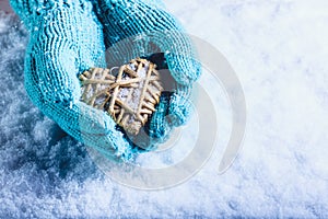 Female hands in light teal knitted mittens with entwined beige flaxen heart on a white snow background. St. Valentines Day concept