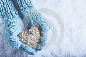 Female hands in light teal knitted mittens with entwined beige flaxen heart on a white snow. Love, St. Valentines Day concept