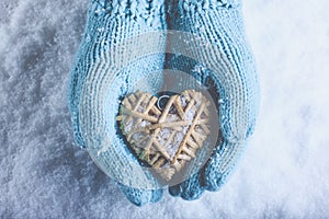 Female hands in light teal knitted mittens with entwined beige flaxen heart on a white snow. Love, St. Valentines Day concept photo