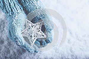 Female hands in light teal knitted mittens with entwined white star on a white snow background. Winter and Christmas concept.