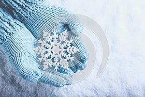 Female hands in light teal knitted mittens with sparkling wonderful snowflake on snow background. Winter and Christmas concept