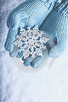 Female hands in light teal knitted mittens with sparkling wonderful snowflake on snow background. Winter and Christmas concept