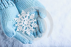 Female hands in light teal knitted mittens with sparkling wonderful snowflake on snow background. Winter and Christmas concept