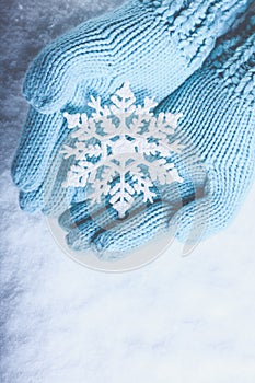 Female hands in light teal knitted mittens with sparkling wonderful snowflake on snow background. Winter and Christmas concept