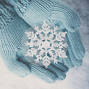 Female hands in light teal knitted mittens with sparkling wonderful snowflake on white snow background. Winter, Christmas concept