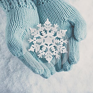 Female hands in light teal knitted mittens with sparkling wonderful snowflake on white snow background. Winter, Christmas concept