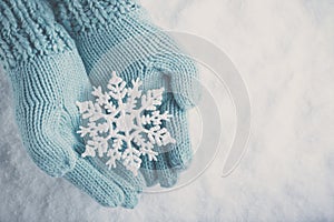 Female hands in light teal knitted mittens with sparkling wonderful snowflake on white snow background. Winter, Christmas concept