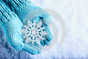 Female hands in light teal knitted mittens with sparkling wonderful snowflake on a white snow background. Winter Christmas concept