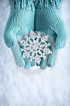 Female hands in light teal knitted mittens with sparkling wonderful snowflake on white snow background. Winter, Christmas concept