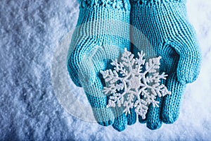 Female hands in light teal knitted mittens with sparkling wonderful snowflake on a white snow background. Winter Christmas concept