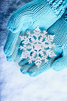 Female hands in light teal knitted mittens with sparkling wonderful snowflake on a white snow background. Winter Christmas concept