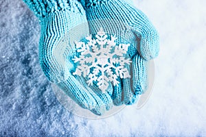 Female hands in light teal knitted mittens with sparkling wonderful snowflake on a white snow background. Winter Christmas concept