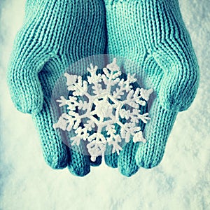 Female hands in light teal knitted mittens with sparkling wonderful snowflake on a white snow. Winter and Christmas concept.