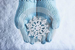 Female hands in light teal knitted mittens with sparkling wonderful snowflake on a white snow. Winter and Christmas concept.