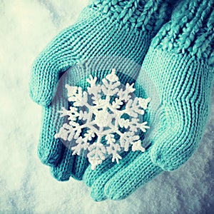 Female hands in light teal knitted mittens with sparkling wonderful snowflake on a white snow. Winter and Christmas concept.