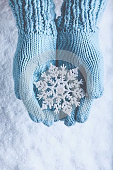 Female hands in light teal knitted mittens with sparkling wonderful snowflake on a white snow. Winter and Christmas concept.