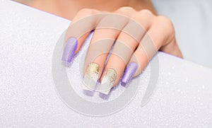 Female hands with long nails with glitter nail polish. Long purple and gold nail design. Women hand with sparkle manicure