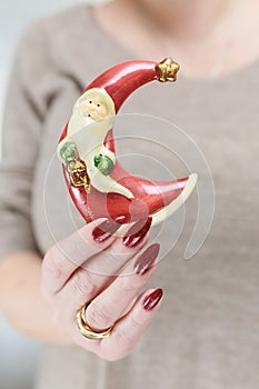 Female hands with long nails and red manicure hold a small statuette of Santa Claus