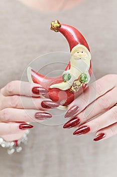 Female hands with long nails and red manicure hold a small statuette of Santa Claus